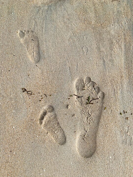 small child footprint on sand with big adult footprint