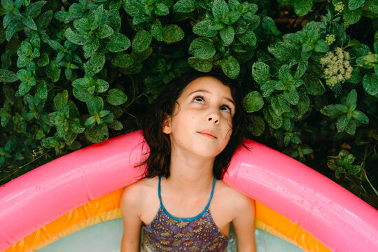 Kid inside inflatable swimming pool leaning on plants