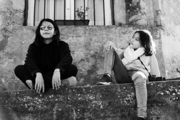 niñas adolescentes hermanas posando sentadas en antigua casa de cemento blanco y negro