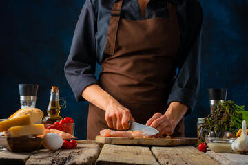 A chef in a dark uniform prepares a Caesar salad. Country style. A rough wooden table on which the...