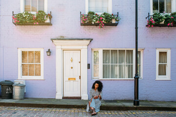 Woman sitting in front of a lilac house facade on the mobile phone