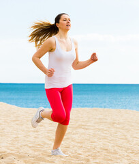 Young fit woman running on beach in sunny morning