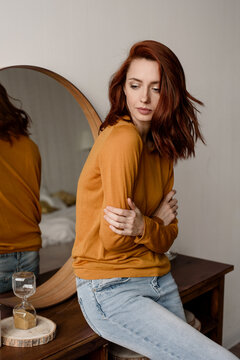 Pensive woman sitting near hourglass at home 