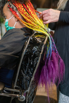 Masked girl getting lomg rainbow box briaids installed
