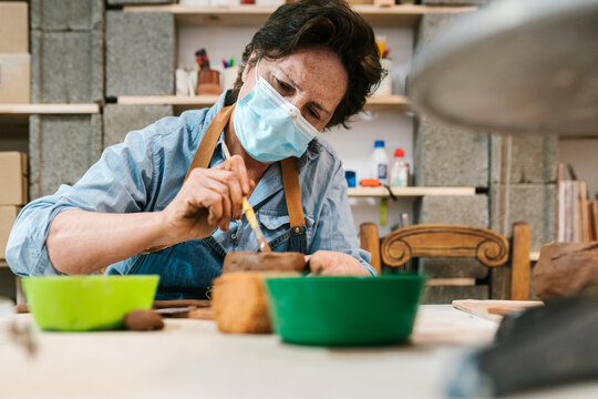 Older potter painting the pot in the pottery workshop - Powered by Adobe