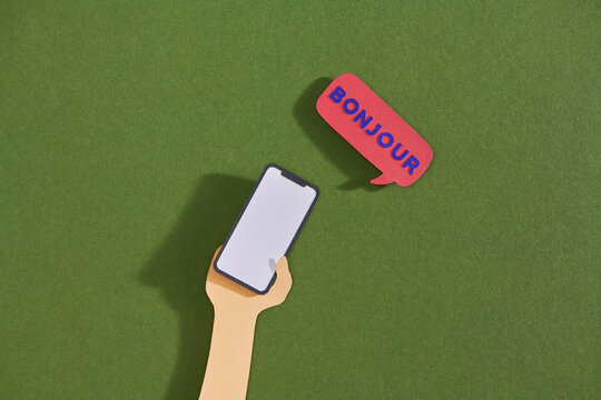 Human hand holding a mobile phone and speech bubble with text bonjour.
