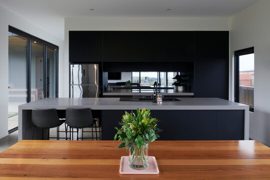 Looking across dining table to large dark styled kitchen