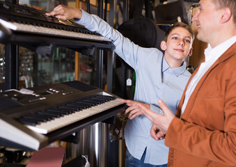 Boy teenager with father looking at synthesizers in the music store