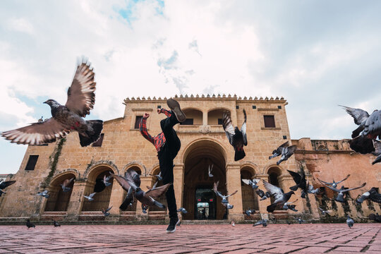Unrecognizable guy doing parkour on square near pigeons
