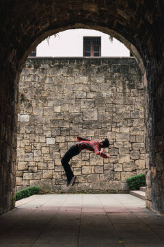 Young man performing back flip on old street