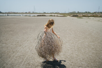 Girl with dry plant playing on the sand