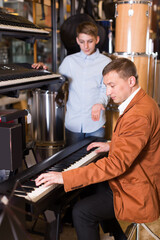Cheerful boy and father deciding on synthesizer in musical shop