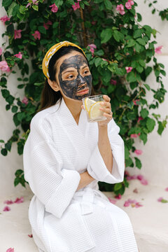 Cheerful Asian female drinking lemon water during spa procedure