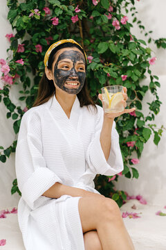 Cheerful Asian female drinking lemon water during spa procedure