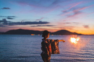 夕暮れの海で花火をする浴衣の女性