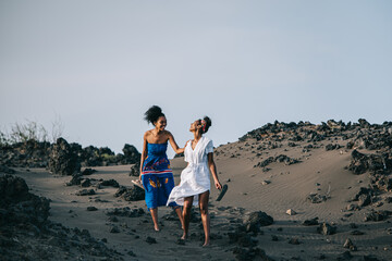 African beautiful sisters walking on volcanic sand dune on the beach beach