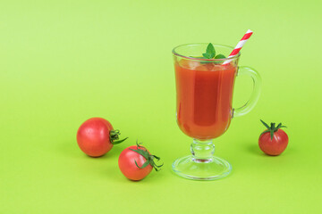 Small tomatoes and a glass of tomato juice on a green background.