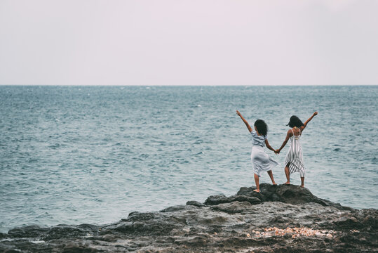 Two sisters standing in a cliff seashore holding hands