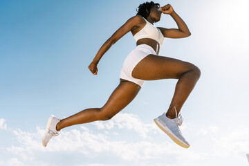 Active black sportswoman jumping against blue sky