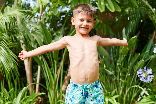 Smiling little boy in shorts standing in his yard