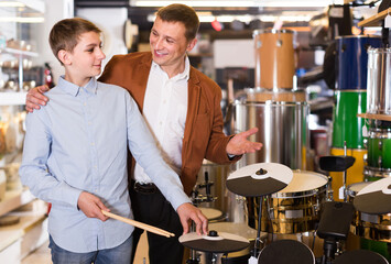 happy european father and teenage son examining drum units in guitar shop