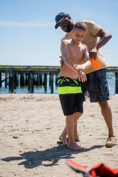 Black father helps son apply sunscreen