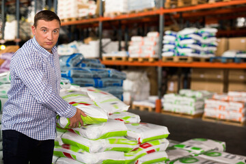 Satisfied cheerful smiling Man choosing compost soil in plastic bags in hypermarket .