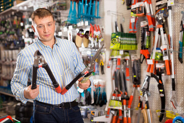 Fototapeta na wymiar Happy positive male customer examining secateurs in garden equipment shop