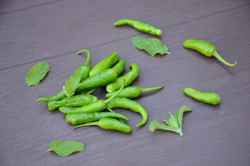closeup the bunch ripe green chilly with mint leaves over out of focus brown background.