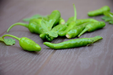 closeup the bunch ripe green chilly with mint leaves over out of focus brown background.