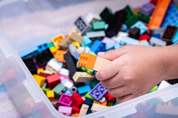 A child's hand is picking up a plastic block connector in a plastic box to play.