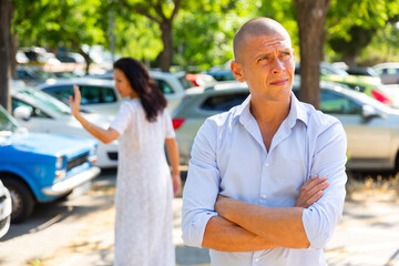 Man and woman having quarrel. Man standing with folded arms and woman brushing off in background.
