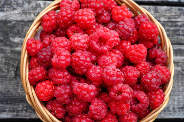 Ripe red raspberries are collected in a wicker basket and stand on a wooden table. top view...