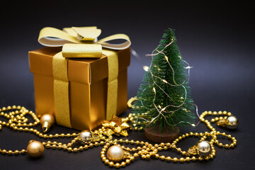 Golden gift at a small christmas tree with balls and beads on a black background