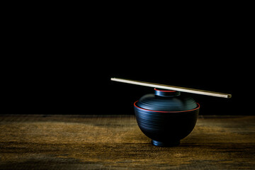 Black cup with chopsticks Japanese style on wooden floor with black background.