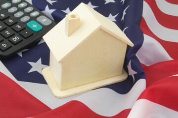 Cost of real estate in USA concept. Calculator and wooden house on United States flag.	