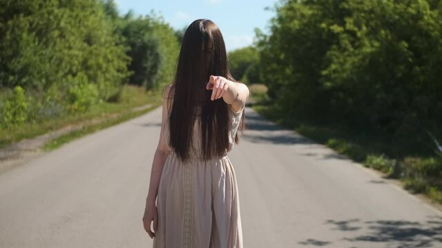 scary ghost woman in an old dress with hair covering her face, shows her finger at the camera. Horror on the road creepy day for travelers.