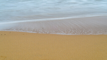 Fototapeta na wymiar The smooth silky waves and seafoam on the sandy beach, long exposure photograph.