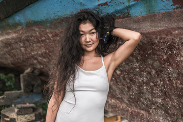 Portrait of beautiful young asian woman wearing white dress and holding hair with hand. Black curly long hair. Looking at camera with copy space.