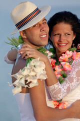 Groom with bride wearing lei, standing under archway on beach (Focus is on bride)