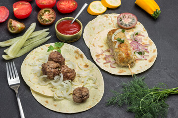 Kebab on skewer and meatballs with tomatoes and onions on pita.