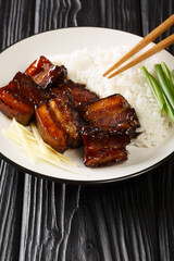 Rafute is a slowly simmered pork with soy sauce black sugar and awamori liquor served with rice closeup in the plate on the table. Vertical