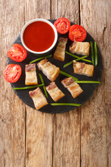 lechon kawali or crispy deep fried pork belly served with sweet and sour sauce closeup in the slate dish on the table. Vertical top view from above