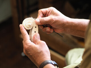 Luthier carving a classic violin head and curl with a small knife in his wrinkled hands