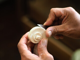Luthier carving a classic violin head and curl with a small knife in his wrinkled hands