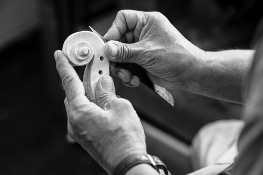Luthier carving a classic violin head and curl with a small knife in his wrinkled hands - Powered by Adobe