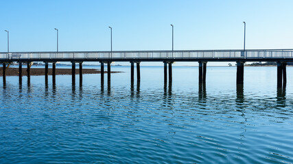 Obraz premium A view of Victoria Point jetty reflected in the rippled water beneath, on a clear blue day