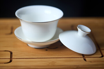 Gaiwan on chaban selective focus. Tea ceremony gong fu cha. Chinese white pottery Dehua white Chinese porcelain gaiwan bowl tea cup and lid with gold border on bamboo teaboard tea tray or chaban.