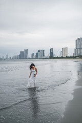 Charming young asian woman in white dress walking on the beach. Romantic photo.