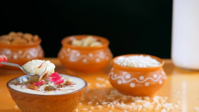Female hand eating a spoonful of tasty rice pudding kept in an earthen bowl. Indian desserts prepared for festival celebration - Kheer  pudding  sevai  sabudana kheer